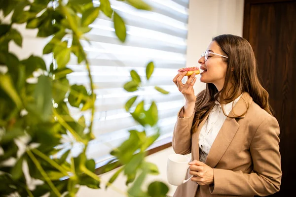 stock image Beautiful woman enjoying the moment and eating delicious donuts at work.