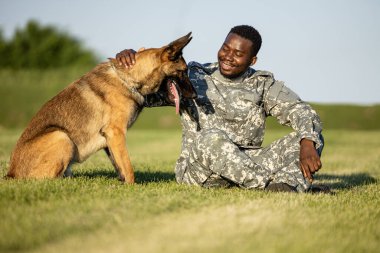 Üniformalı asker askeri köpeğiyle oynuyor ve eğleniyor..