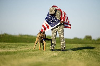 Amerikan askeri askeri askeri köpeğinin yanında duruyor ve elinde bayrak var..