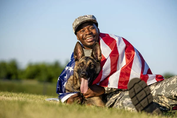 American pride. Soldier in military uniform carrying USA flag and embracing his dog.