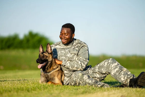 Military working dog and soldier lying on the grass and embracing.