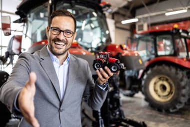 Traktör satıcısı atölyede duruyor ve tarım makinelerinin yedek parça ve hizmetlerini garanti ediyor.
