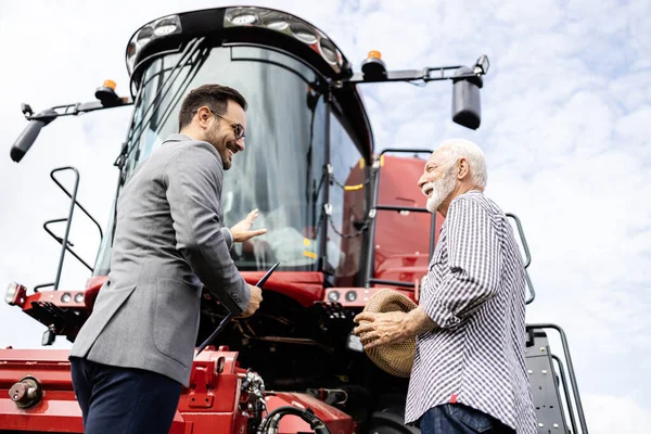 Salesman and farmer discussing about new combine harvester. Buying tractors and agricultural machines.
