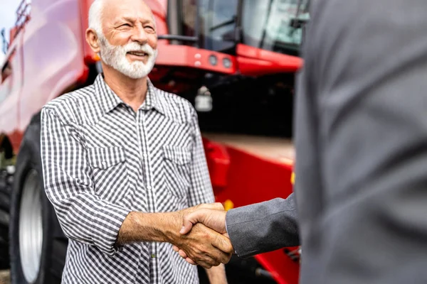 Dealership salesman and farmer handshake in front of brand new tractor. Buying agricultural machines.