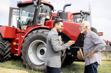 Çiftçi tarım fuarında yeni traktörü test ediyor. Satıcı tarım makineleri satıyor..