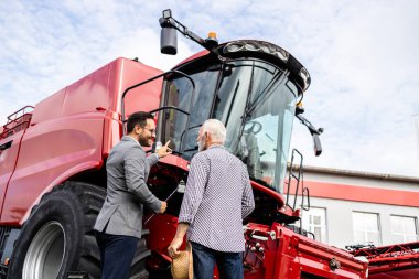 Traktör satıcısı çiftçiye yeni tarım ekipmanları gösteriyor..