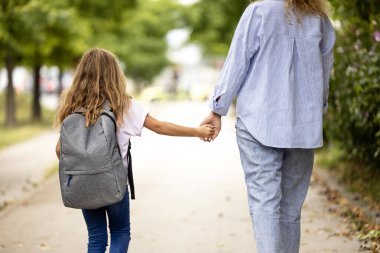 Anne ve kız el ele tutuşup okula doğru yürüyorlar..
