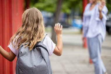 Okul çantalı kız okula girerken annesine el sallıyor.. 