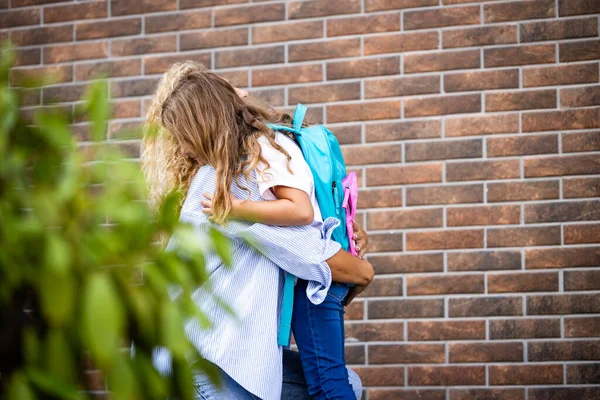 Anne ve kızı okula gitmeden önce kucaklaşıp öpüşüyorlar. Ebeveynler ve çocuklar arasında sevgi.
