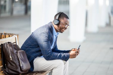 Zarif takım elbiseli yakışıklı adam müzik dinliyor ve şehirde akıllı telefon kullanıyor..