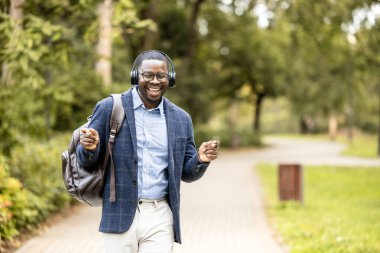 Kulaklıklı, müzik dinleyen, yürürken şarkı söyleyen ve dans eden mutlu bir adam..