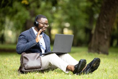 Ofis dışında çalışan bir iş adamı. Parkta çimlerde oturmak ve dizüstü bilgisayarla çalışmak..