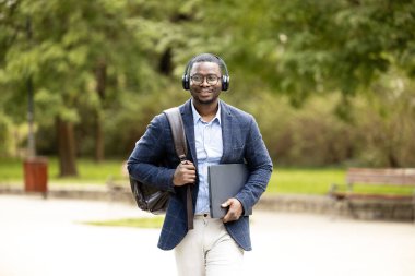 İşe giderken yanında çanta ve laptop taşıyan takım elbiseli bir adamın portresi.