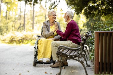 Tekerlekli sandalyede oturan yaşlı bir adam ve yaşlı bir kadın boş zamanlarının ve emekliliğinin tadını çıkarıyorlar..