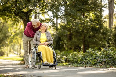 Tekerlekli sandalyede oturan yaşlı bir adam ve yaşlı bir kadın boş zamanlarının ve emekliliğinin tadını çıkarıyorlar..