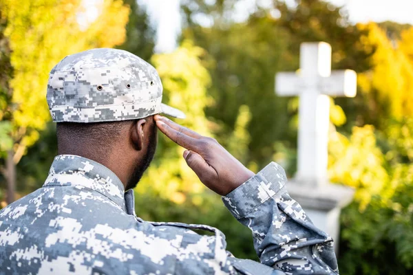 Soldier in military uniform at cemetery saluting to his fallen comrades.