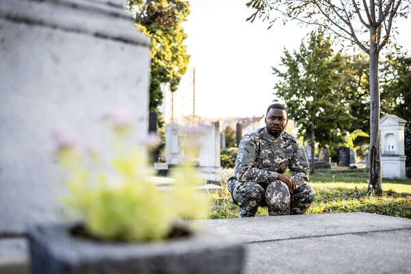 Soldier in military uniform at cemetery kneeling in front of his friend's grave feeling sorrow and pain.