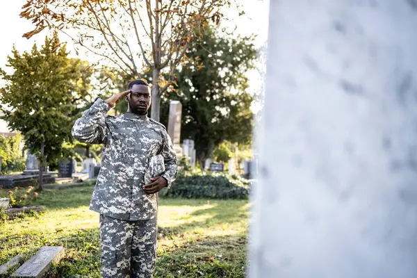 Soldier in military uniform at cemetery saluting in honor to fallen war heroes.