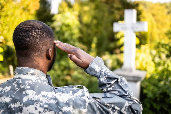 Soldier in military uniform at cemetery saluting in honor to fallen war heroes.