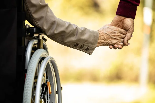 Care for elderly people. Unrecognizable senior woman in wheelchair holding hands with senior man. Nursing home concept.