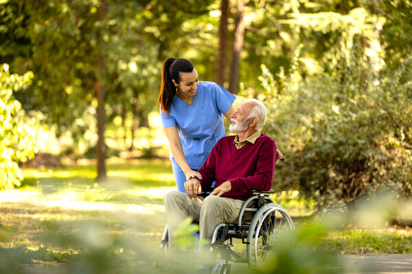 Nurse and elderly man in wheelchair going for a walk in the park.