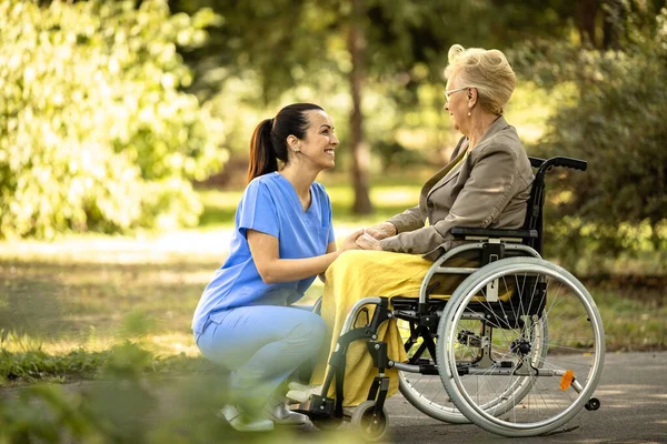 Female nursing assistant taking care of elderly woman in wheelchair.