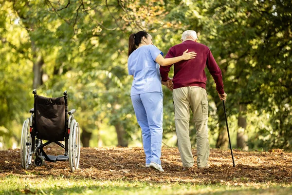 Nursing assistant helping elderly man to walk with walking cane.
