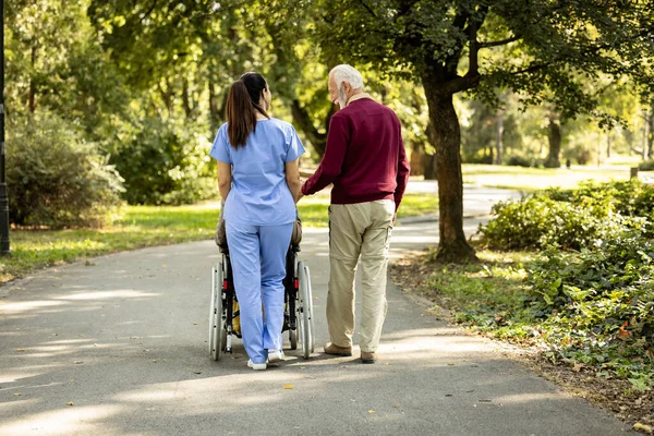 Nursing assistant and senior people walking together in the park.