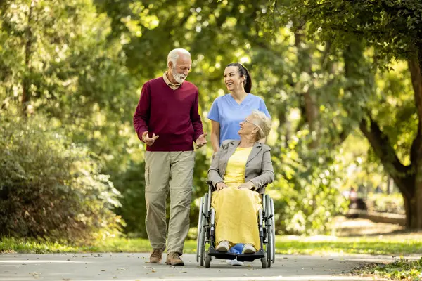 Nursing assistant, senior man and elderly woman in wheelchair enjoying the walk in park.
