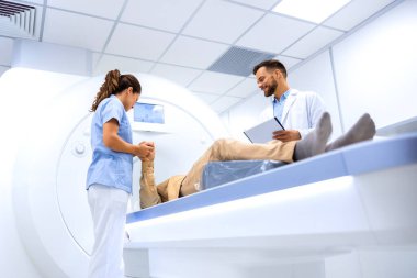 Tıbbi muayene odasında MR çekilirken kıdemli hastaya yardımcı olan kadın doktor..