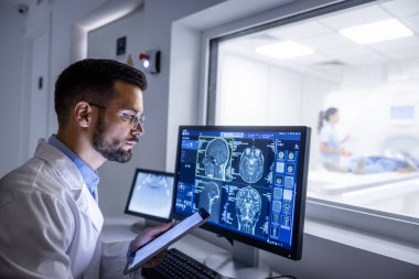 Doktor MRI kontrol odasında röntgen görüntülerini incelerken arka plan hemşiresi hastayı muayene testine hazırlıyor..