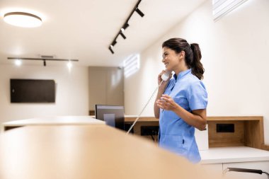 Hastane resepsiyonisti telefonla konuşuyor ve doktor randevusu alıyor..