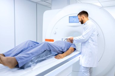 Radyolog veya teknisyen kıdemli adamı onkoloji teşhis merkezinde tam MRI veya CT kafa taraması için hazırlıyor..