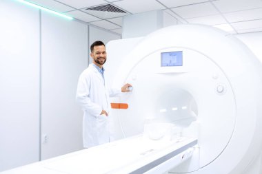 Pozitif doktor radyoloğun portresi hastanede modern MRI tarama makinesinin yanında duruyor.. .