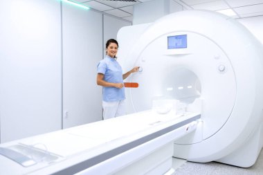 Kadın radyolog hastanede modern MRI tarama makinesinin yanında duruyor..