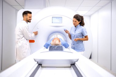 Radyolog ve bayan teknisyen hastayı hastane teşhis odasında MRI prosedürüne hazırlıyorlar..