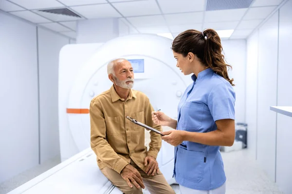 Female radiologist preparing and encouraging senior man before MRI or CT procedure in hospital.