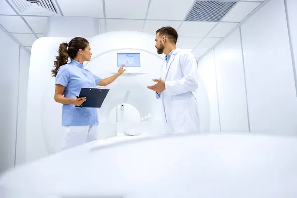 Doctor radiologist and female technician preparing MRI scan in medical examination room.