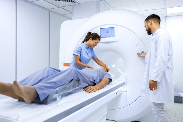 Female doctor assisting senior patient while doing MRI scan in medical examination room.