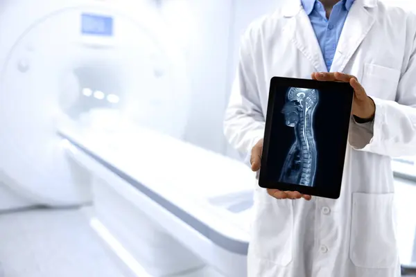 Doctor radiologist standing in MRI medical examination room and showing X-ray image of patient body.