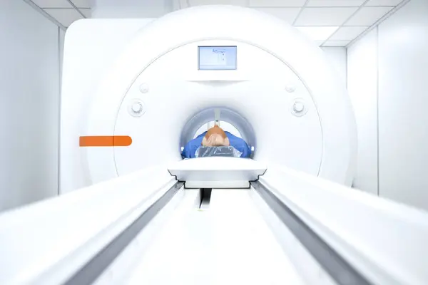Patient lying down inside a medical scanner in hospital MRI examination room.