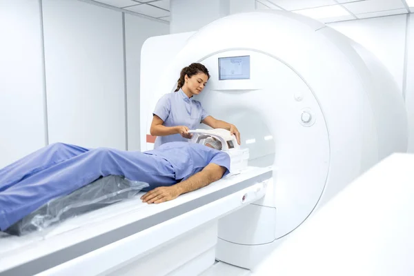 Female radiologist or technician preparing senior man for complete MRI or CT head scan at oncology diagnostic center.