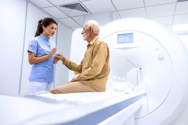 Female radiologist or technician preparing senior man for complete MRI or CT head scan at oncology diagnostic center.