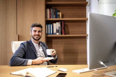 Gülümseyen yakışıklı iş adamının portresi ofisinde oturuyor ve elinde bir fincan kahve tutuyor..