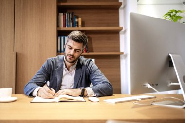 Şık takım elbiseli konsantre beyaz iş adamı lüks ofisinde evrak işleriyle uğraşıyor..