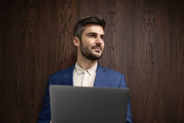 Şirket içinde dizüstü bilgisayar tutan takım elbiseli şık bir adamın portresi..