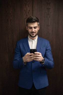 Şık takım elbiseli bir adam şirket içinde akıllı telefon kullanıyor..