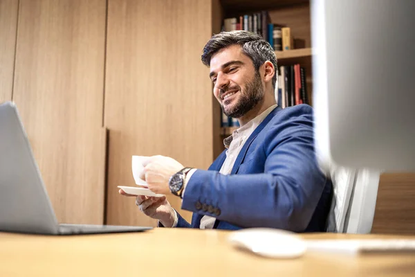 Handsome caucasian company director enjoying cup of coffee in modern hardwood luxurious office.