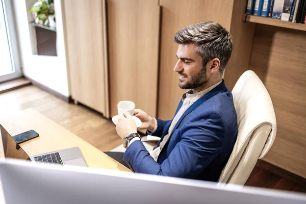 Relaxed man in business suit enjoying cup of coffee in the office.
