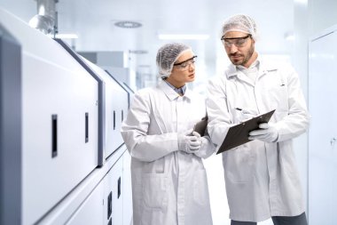 Deneyimli teknoloji uzmanları modern endüstriyel makinenin yanında duruyor ve üretim sonuçlarını analiz ediyorlar..